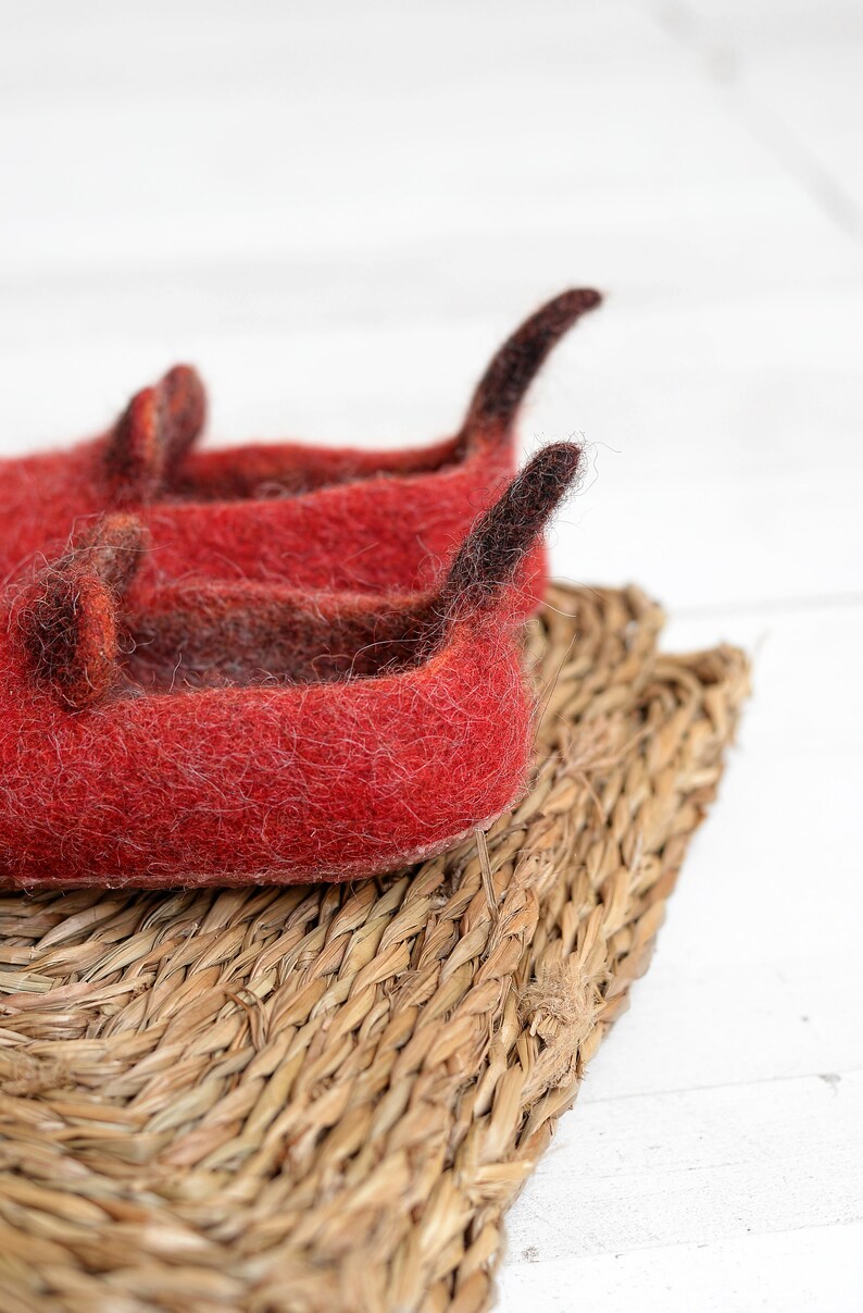 May include: Two red felt slippers with black felt accents. The slippers are sitting on a woven straw mat.