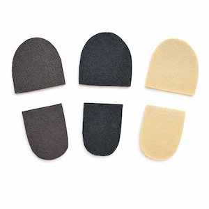 Op de afbeelding: Zes hielinzetstukken voor schoenen in drie kleuren: donkerbruin, zwart en beige. De inzetstukken zijn halfrond met een getextureerd oppervlak, ontworpen om in schoenen te passen voor extra comfort en ondersteuning.