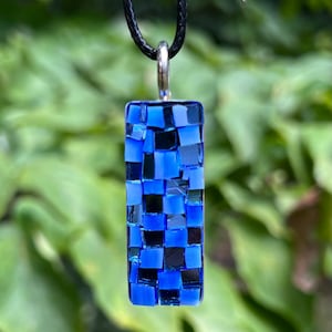 May include: A blue and black mosaic glass pendant necklace. The pendant is rectangular and hangs from a black cord.
