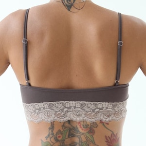 May include: A woman with a tattoo of a Hindu deity on her lower back, wearing a brown lace-trimmed bra and brown pants.