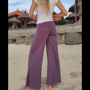 May include: A woman wearing a white top and wide-legged pants in a deep purple shade. The pants are made of a soft, flowing fabric and have a relaxed fit.