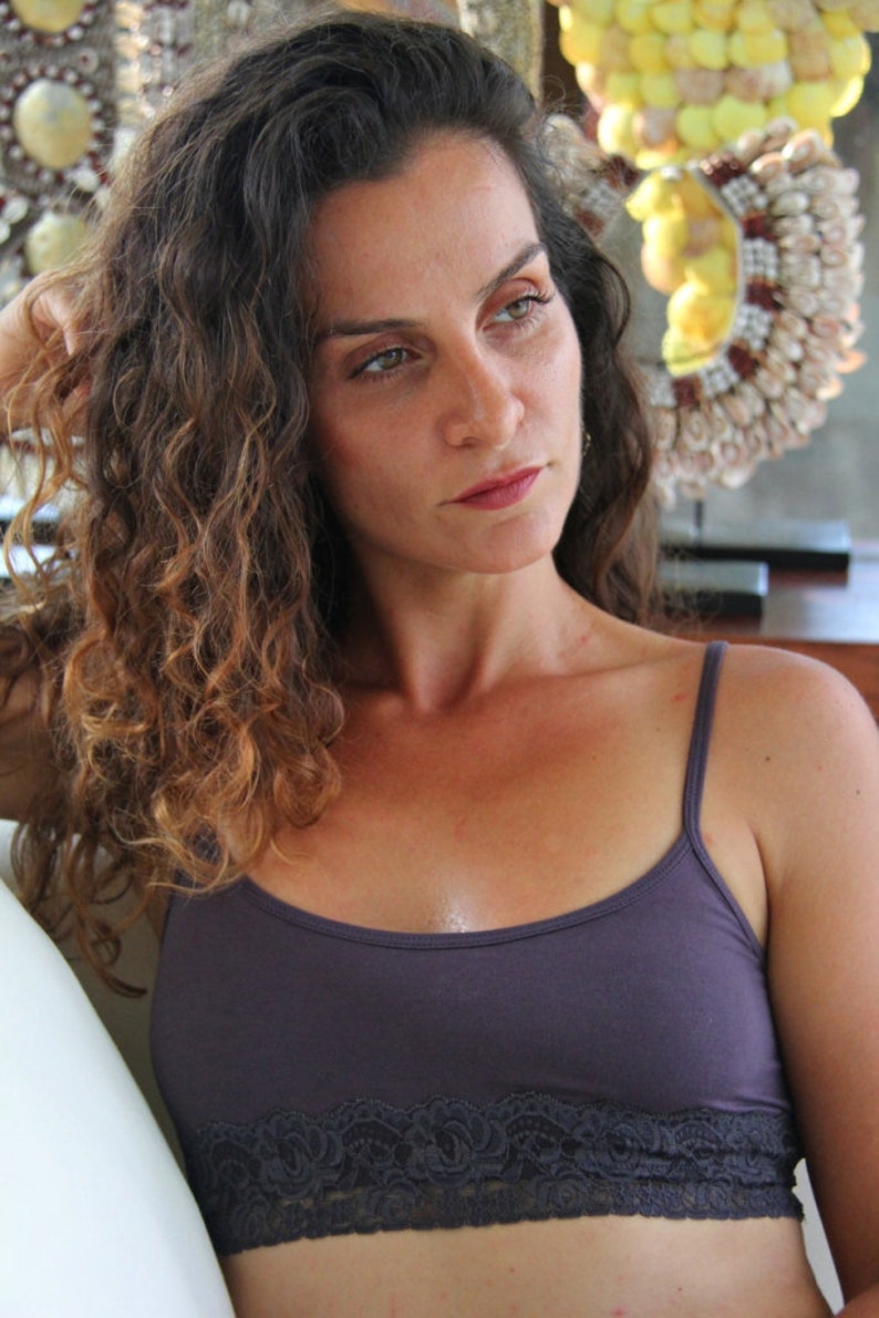 May include: A woman with long, curly brown hair is wearing a dark purple tank top with a black lace trim. The tank top has thin straps.