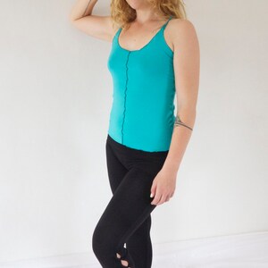 May include: A woman wearing a turquoise tank top and black cropped leggings with cutouts on the lower legs.