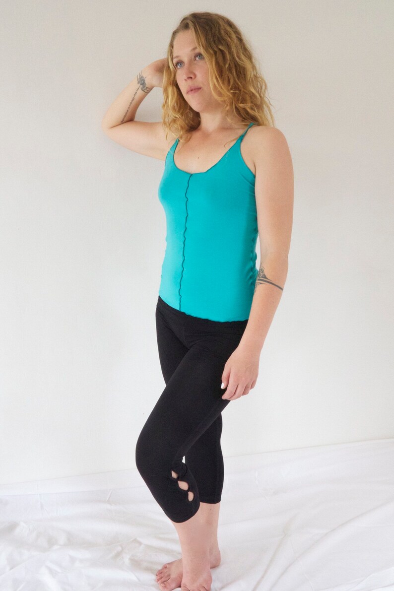 May include: A woman wearing a turquoise tank top and black cropped leggings with cutouts on the lower legs.