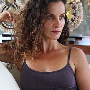 May include: A woman with long, curly brown hair is wearing a dark purple, lace-trimmed tank top. She is looking off to the side.
