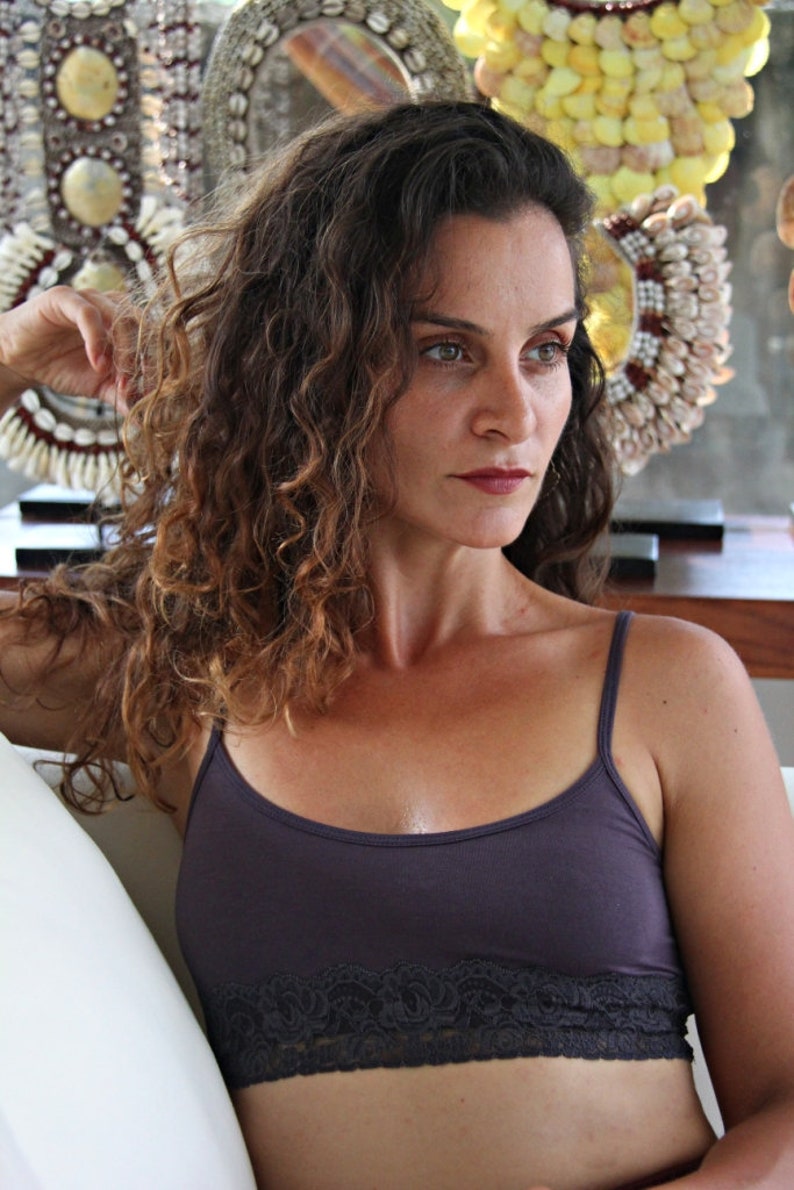 May include: A woman with long, curly brown hair is wearing a dark purple, lace-trimmed tank top. She is looking off to the side.