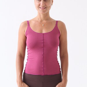 May include: A woman wearing a pink tank top and brown leggings. She is standing with her hands on her hips and looking to the side.