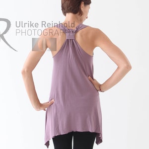 May include: A woman wearing a mauve tank top with a knotted back detail and black leggings. The top has a slightly asymmetrical hemline.