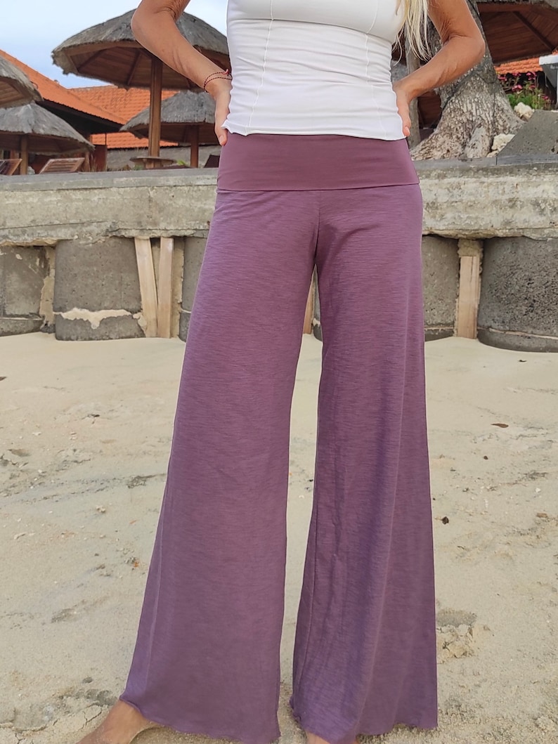 May include: Wide-leg pants in a deep purple color with a wide waistband. The pants are made of a soft, flowing fabric.