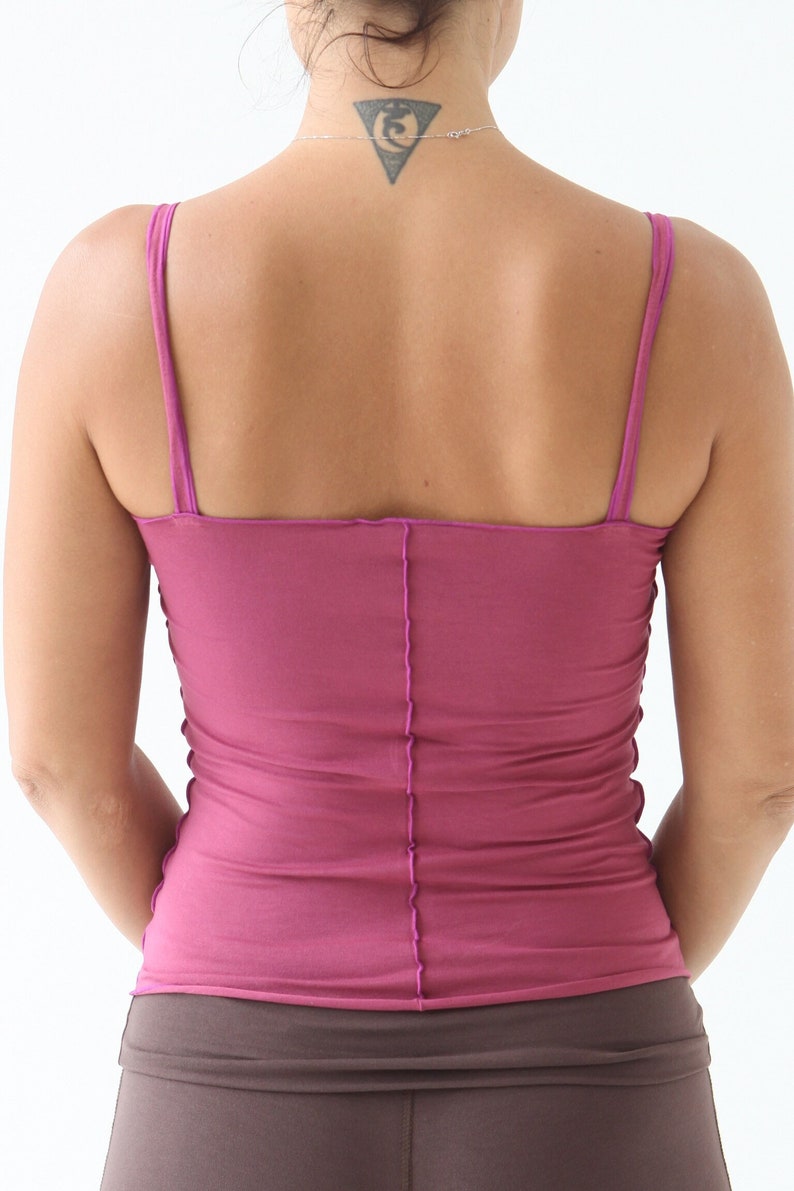 May include: A close-up of a woman wearing a pink tank top with thin straps. The tank top is made of a soft, stretchy fabric and has a fitted silhouette. The woman is wearing a brown skirt.