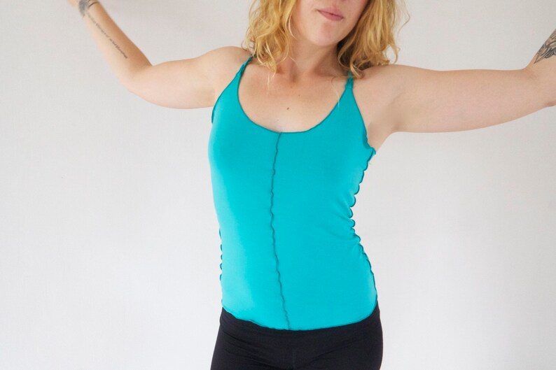 May include: A turquoise tank top with thin straps and a straight neckline. The top has a seam down the center front.