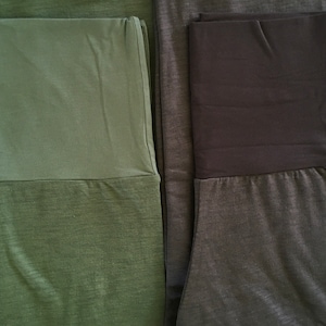 May include: Two pairs of leggings with a contrasting waistband. One pair is green with a dark green waistband, and the other pair is gray with a black waistband.