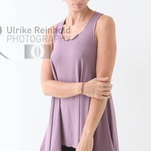 May include: A woman wearing a mauve sleeveless top with a flowing asymmetrical hem. The top is made of a soft, comfortable fabric and has a relaxed fit.