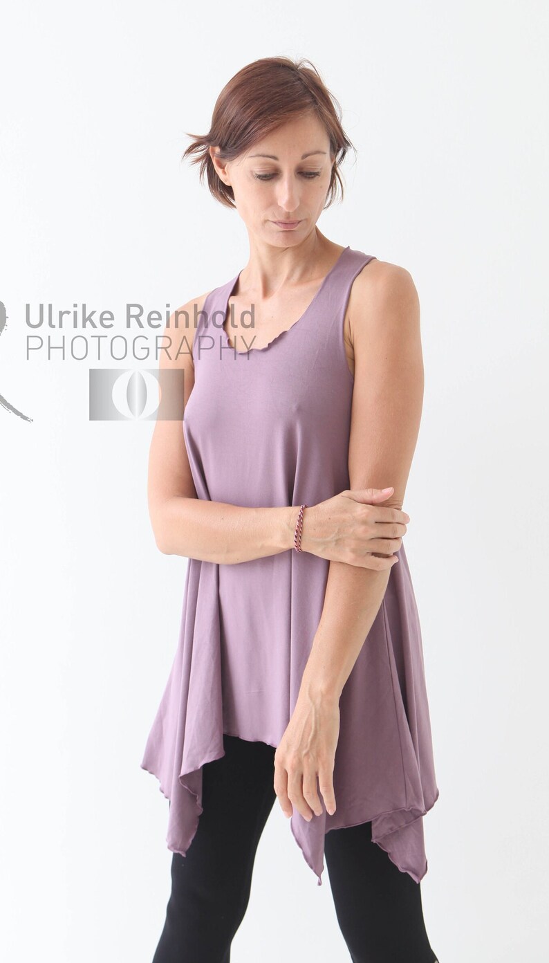 May include: A woman wearing a mauve sleeveless top with a flowing asymmetrical hem. The top is made of a soft, comfortable fabric and has a relaxed fit.