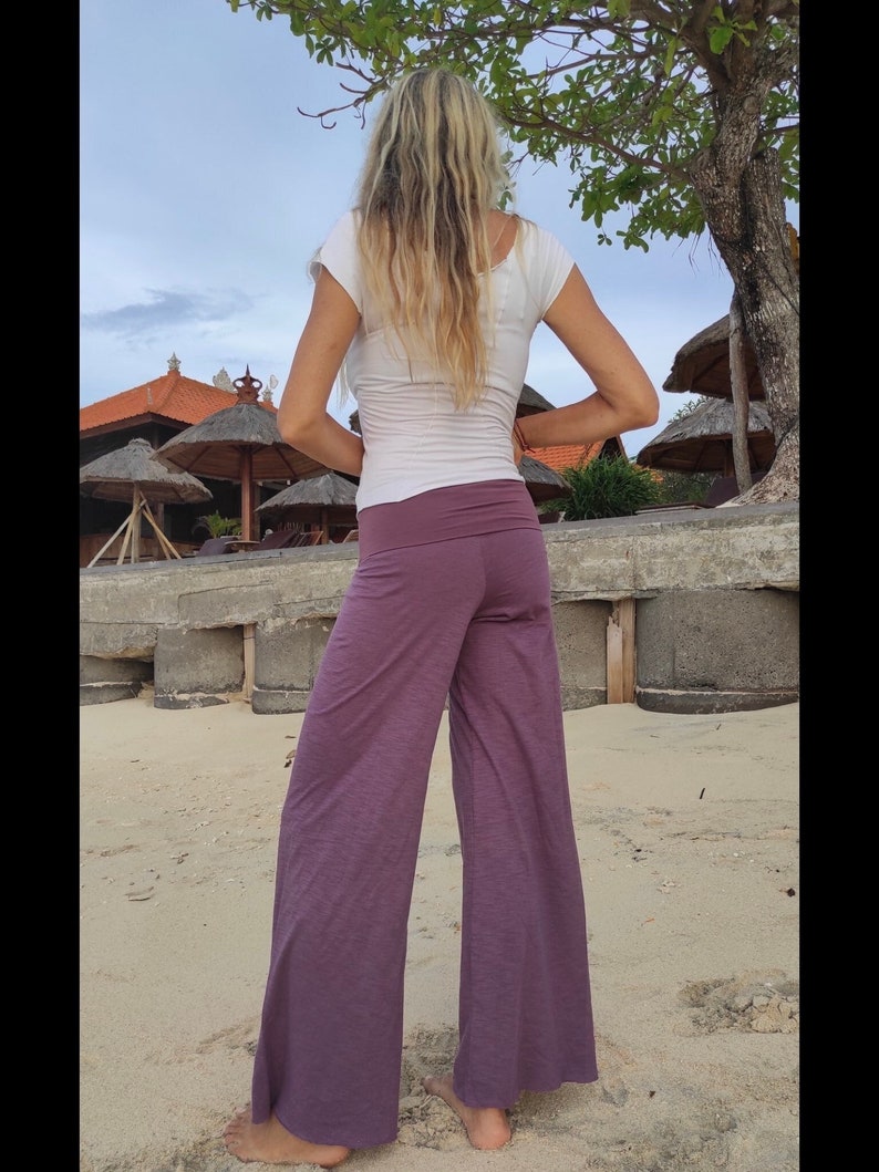 May include: A woman wearing a white top and wide-legged pants in a deep purple shade. The pants are made of a soft, flowing fabric and have a relaxed fit.