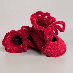 May include: A pair of red crocheted baby booties with a ruffled trim and a bow detail.