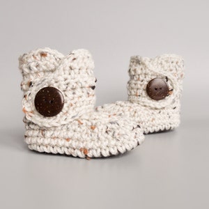 May include: A pair of cream-colored crocheted baby booties with brown wooden buttons.