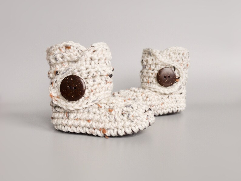 May include: A pair of cream-colored crocheted baby booties with brown wooden buttons.