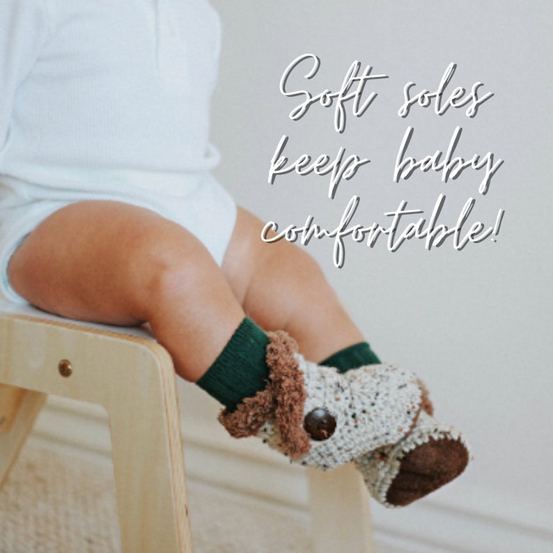 May include: A baby's legs are shown, wearing green socks and crocheted booties. The booties are beige with brown accents and a wooden button. The text "Soft soles keep baby comfortable!" is overlaid on the image.