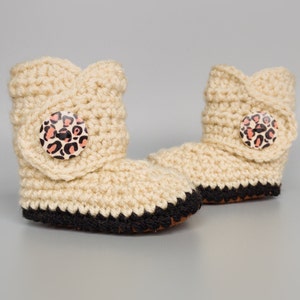 May include: A pair of beige crocheted baby booties with black trim and leopard print buttons.