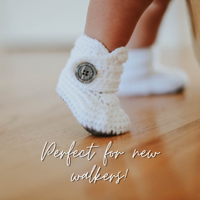 May include: White crocheted baby booties with a button closure. The booties are on a wooden floor. "Perfect for new walkers!" is written on the floor.