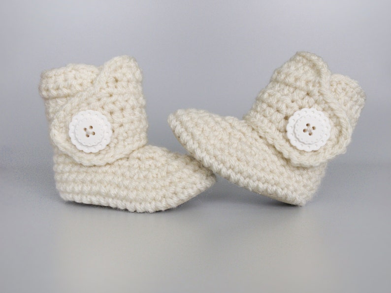 Puede incluir: Un par de botines de beb&eacute; de ganchillo de color crema con botones blancos.