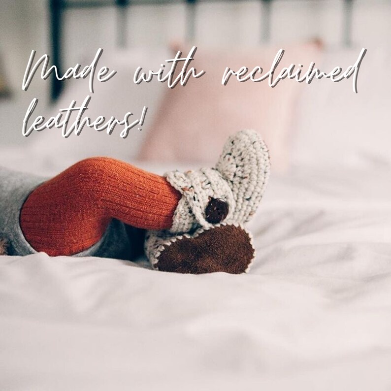 May include: A baby's feet wearing white and brown crocheted booties with a brown leather sole. The booties are made with reclaimed leathers. The baby is lying on a white bed.