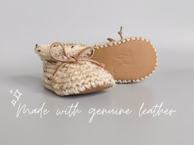 May include: A pair of beige crocheted baby booties with brown leather laces and soles. The booties are made with genuine leather and have a soft, comfortable feel.