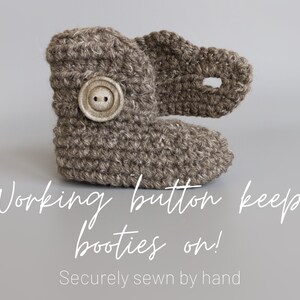 May include: Brown crocheted baby booties with a button closure. The text "Working button keeps booties on! Securely sewn by hand" is below the booties.