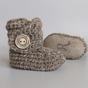 May include: A pair of brown crocheted baby booties with a button on the top. One bootie has a suede sole with the letter "R" embossed on it.