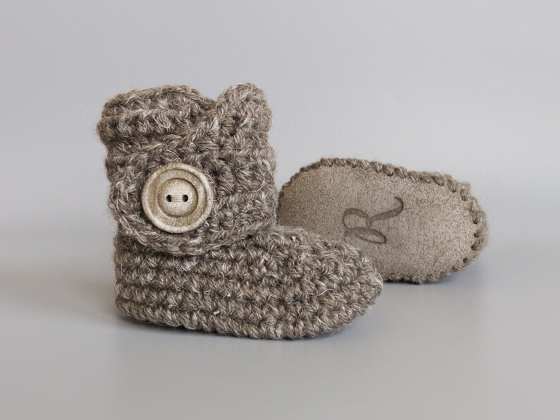 May include: A pair of brown crocheted baby booties with a button on the top. One bootie has a suede sole with the letter "R" embossed on it.