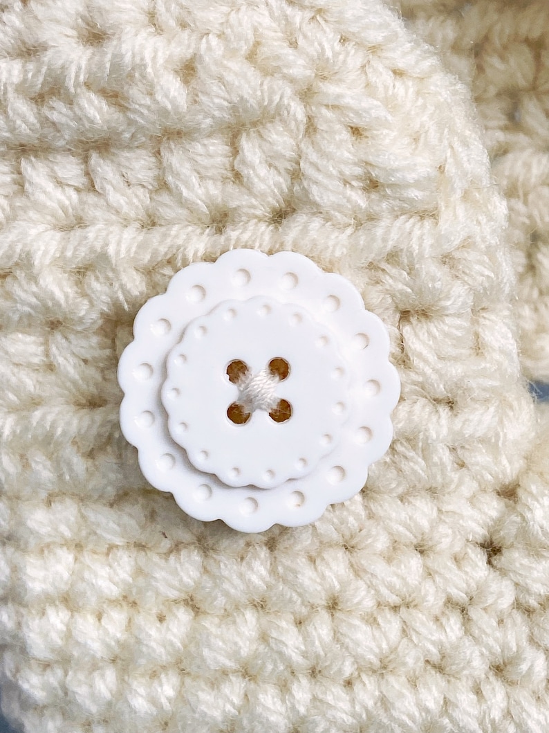 Puede incluir: Una tela de crochet blanca con un bot&oacute;n de pl&aacute;stico blanco con borde festoneado.