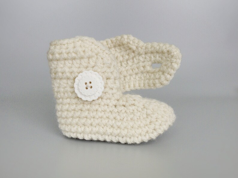 Puede incluir: Zapatillas de beb&eacute; de ganchillo de color crema con un bot&oacute;n blanco.
