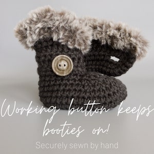 May include: A dark gray crocheted baby bootie with a faux fur trim. A large, round, tan button secures the bootie. The text "Working button keeps booties on!" is visible.