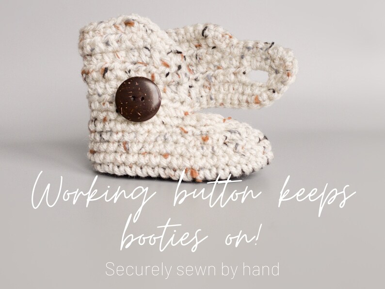May include: Cream-colored crocheted baby booties with a brown wooden button. The text "Working button keeps booties on! Securely sewn by hand" is below the booties.