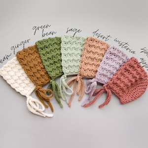 May include: Seven crocheted baby bonnets in different colours, including cream, ginger, green bean, sage, desert, wisteria, and spiced apple.
