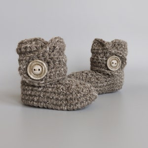 May include: A pair of brown crocheted baby booties with a button on each. The booties are made with a soft, textured yarn.