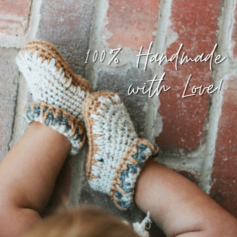 May include: A pair of crocheted baby booties in white, brown, and gray with the text "100% Handmade with Love!"
