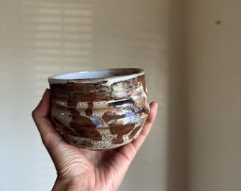 Taza de cerámica artesanal con diseño en espiral, rojo, marrón y blanco, taza de arcilla texturizada, tonos tierra.