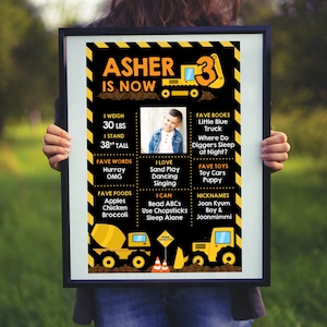 Könnte beinhalten: Ein gerahmtes Geburtstagsplakat mit schwarzem Rand, mit einem Foto eines jungen Jungen und Grafiken zum Thema Bau. Das Plakat enthält den Text "Asher is Now 3", Gewicht 13.6 kg, Größe 96.5 cm, Lieblingsdinge und Spitznamen.