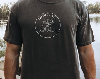 May include: Dark gray t-shirt with a white circular graphic. The graphic features a line drawing of a fish jumping out of the water, with the words "FISHER OF MEN" and "MATT. 4:19" in a circular design. The shirt is short-sleeved.