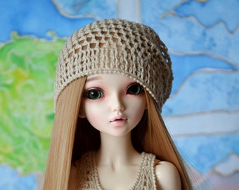 Peut inclure: Une poupée articulée aux longs cheveux blonds raides, portant un bonnet en crochet beige et un haut sans manches en crochet beige assorti avec trois petits boutons couleur bronze à l'encolure, associé à un short en jean bleu clair usé.
