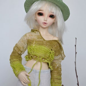 Peut inclure: Une poup&eacute;e portant un chapeau crochet&eacute; vert, un haut crochet&eacute; vert et marron et un pantalon gris.