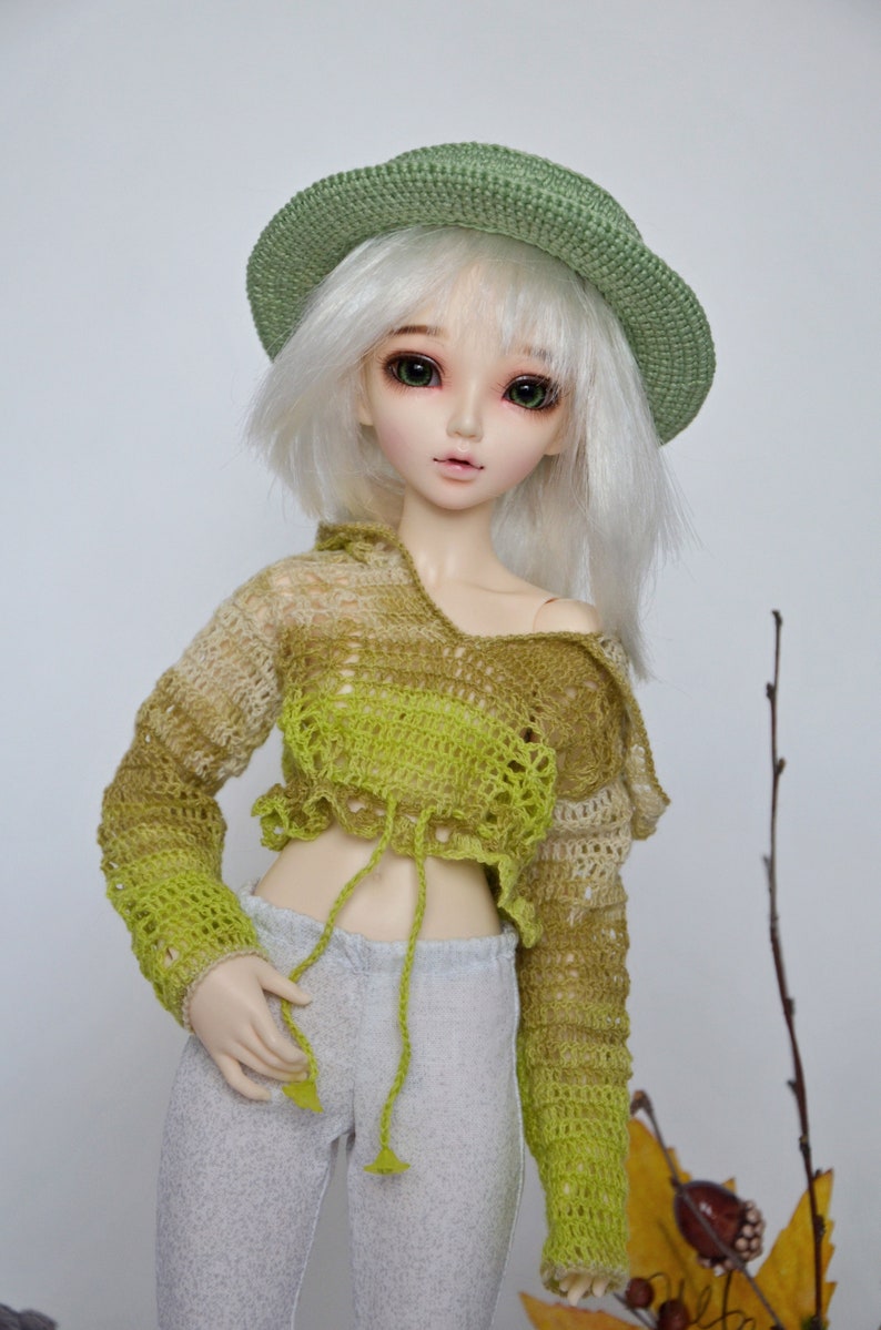 Peut inclure: Une poup&eacute;e portant un chapeau crochet&eacute; vert, un haut crochet&eacute; vert et marron et un pantalon gris.