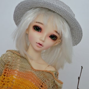 Peut inclure: Une poup&eacute;e aux cheveux blancs et aux yeux verts portant un chapeau crochet&eacute; gris et un haut crochet&eacute; multicolore.