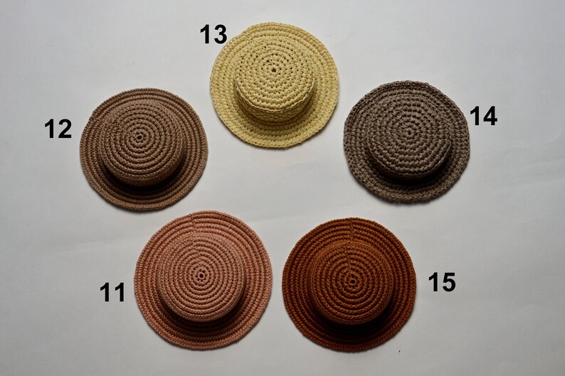 Peut inclure: Cinq chapeaux en crochet de diff&eacute;rentes couleurs, dont le marron, le beige, le brun clair et le rose. Les chapeaux sont dispos&eacute;s en cercle sur un fond blanc.