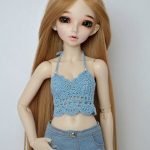 May include: A doll with long, light brown hair and green eyes wears a light blue crochet halter top and denim shorts. The shorts have a button closure and distressed detailing. The doll is posed against a white background.
