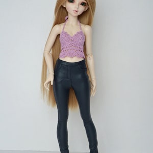 May include: A doll with long blonde hair wearing a lavender crochet halter top and dark blue faux leather pants. The doll has green eyes and is standing against a white background.