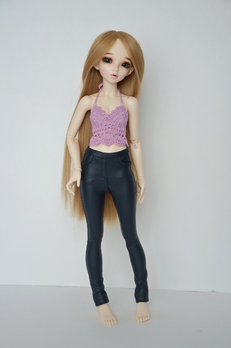 May include: A doll with long blonde hair wearing a lavender crochet halter top and dark blue faux leather pants. The doll has green eyes and is standing against a white background.