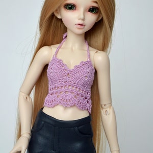 May include: A doll with long, light brown hair and green eyes is wearing a lavender crochet halter top and black pants. The doll is posed against a plain white background.